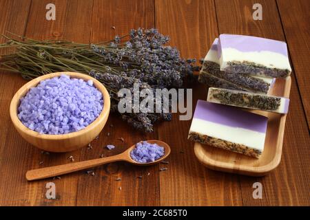 Meersalz mit Lavendel in einer Bambusschale befinden sich Seife aus Lavendel, Olivenöl und Kakaobutter auf einem Bambusteller und getrocknete Lavendelblüten Stockfoto