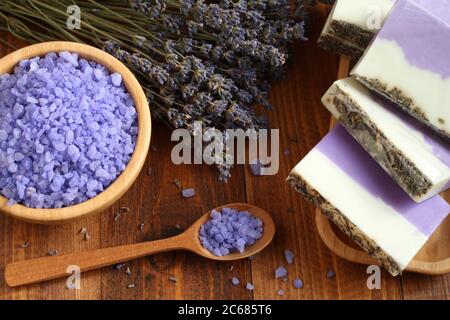 Meersalz mit Lavendel in einer Bambusschale befinden sich Seife aus Lavendel, Olivenöl und Kakaobutter auf einem Bambusteller und getrocknete Lavendelblüten Stockfoto