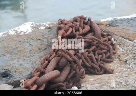 Nahaufnahme der Rusty-Kette, die auf der Andockseite liegt, mit Wasser im Hintergrund Stockfoto