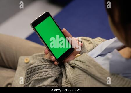 Über der Schulter einer jungen Frau hält grünen Bildschirm Smartphone, sitzt auf dem Sofa zu Hause. Weichzeichnen Hintergrund Stockfoto