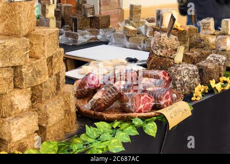 Verschiedene italienische Käsesorten und typische Salami zum Verkauf auf einem Straßenmarkt im mittelalterlichen Dorf Asciano in Siena, Toskana in Italien Stockfoto