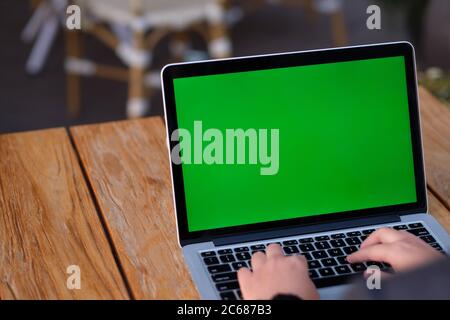 Über die Schulter der Menschen mit grünen Bildschirm Laptop-Computer auf Holztisch. Weichzeichnen Hintergrund Stockfoto