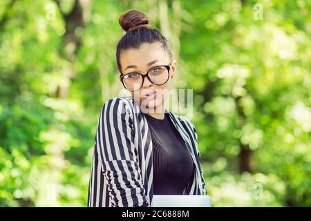 Junge attraktive Mädchen mit Brille. Frau mit Laptop, in einem Stadtpark auf einem grünen Natur Hintergrund im Freien. Freiberufliches Geschäftskonzept. Lustige Emoti Stockfoto