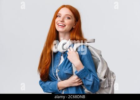 Hochschulleben, modernes Lifestyle- und Bildungskonzept. Fröhliche, gut aussehende Rothirnschin mit foxy langen Haaren, Kopfhörer über dem Hals Stockfoto