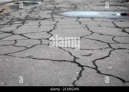 Rissige, nasse Asphaltdecke. Verkehr, Straßenreparaturen, Wetter und schlechte Qualität Konzept. Städtische Umwelt Stockfoto