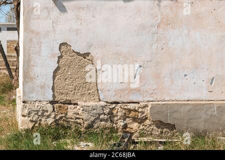 Der Putz blättert von der Ziegelwand. Die Gründung eines Wohnhauses bricht allmählich zusammen. Stockfoto