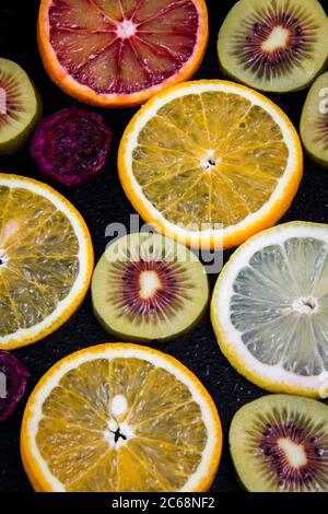 Runde Scheiben von roten und gelben Orangen und roten Kiwis auf schwarzem Hintergrund. Stockfoto