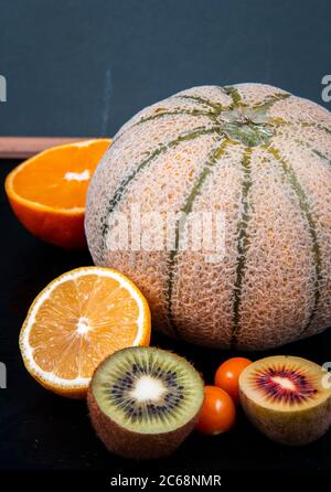 Gehackte grüne und goldene Kiwis, orangefarbene Hälften, Honigmelonen und chinesische Laternen Früchte. Stockfoto