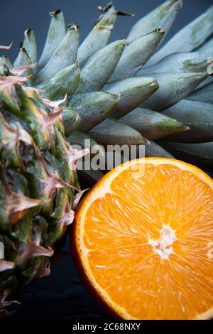 Dünne Scheiben Orange und Kiwi in der Nähe einer großen frischen Ananas auf schwarzem Hintergrund. Stockfoto