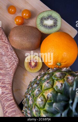 Eine Ananas, eine volle Orange und Kiwi, zwei Kiwi Hälften und einige chinesische Laternen Früchte auf einem Schneidebrett. Stockfoto