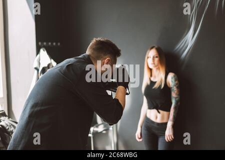 Tattoo-Meister, die Fotos auf Kamera von tätowierten Mädchen auf schwarzem Hintergrund in modernen Studio Stockfoto
