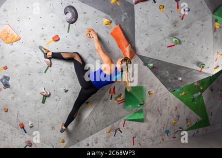 Kletterer Frau hängt an einer Boulderkletterwand, innen an farbigen Haken. Stockfoto