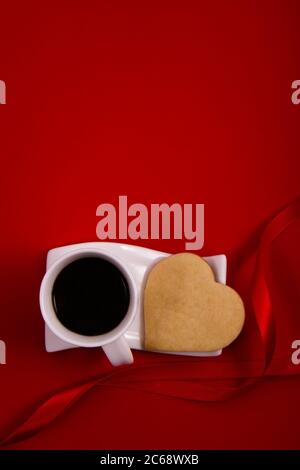 Das Herz des Keks ist neben einer Tasse Kaffee mit rotem Hintergrund und Valentinstag Stockfoto