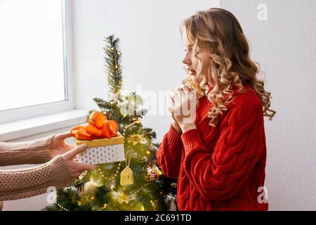 Mädchen in roten Pullover wird von einem weihnachts-Geschenkbox mit einer großen roten Schleife überrascht. Weihnachtsbaum auf Hintergrund. Stockfoto