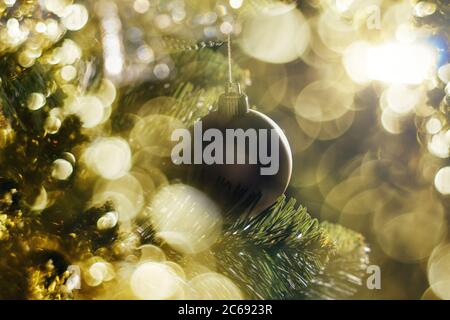 Braune weihnachtskugel hängt an einem Zweig. Dekorationen auf dem weihnachtsbaum. Goldenes Bokeh um Ball. Weihnachten und Neujahr Konzept. Stockfoto