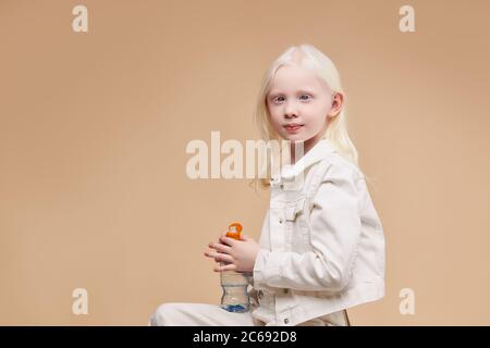 Seitenansicht auf wunderschöne Ruhe und schüchtern Albino Kind sitzt mit Wasserflasche isoliert. Modell mit ungewöhnlichen blasse Haut, weiße Haarfarbe und blauen Augen aussehen Stockfoto