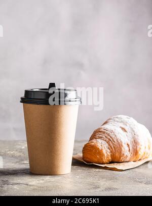 Papiertasse mit Kaffeegetränk oder Tee frisches knuspriges Croissant auf grauem Hintergrund. Null-West-Konzept für Speisen und Getränke. Stockfoto