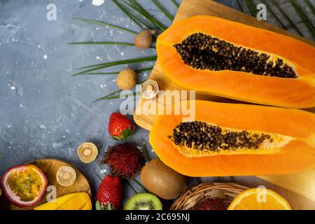 Papaya. Tropische Früchte. Nahaufnahme von zwei Hälften reifer Papaya mit Samen auf Holzschneidebrett. Papaya in Scheiben und andere exotische Früchte auf dem Tisch Stockfoto