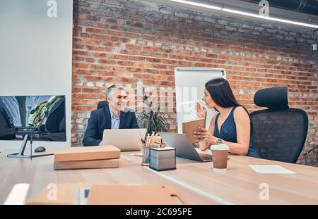 Zwei lächelnde Mitarbeiter sitzen am Holztisch Stockfoto