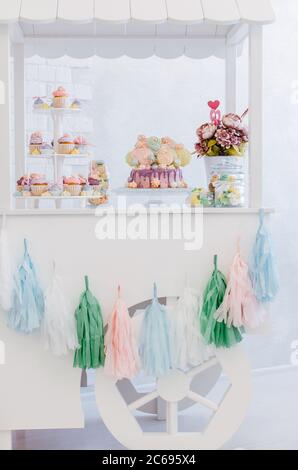Bonbon Bar Cart mit Geburtstagskuchen, Tasse Kuchen und Baiser auf einem hellen Hintergrund. Gelb, lila, blau, grün, rosa Farben. Stockfoto