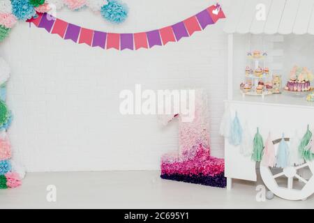 Dekorierter Bereich für den ersten Baby Geburtstag mit einer weißen Steinwand auf dem Hintergrund. Für Mädchen Fotoession. Bonbon Bar, rosa Nummer eins und Fahnen Girlande. Stockfoto
