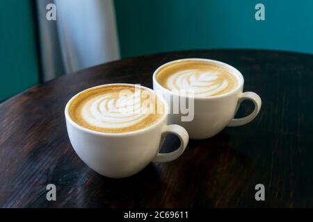 Zwei Tassen Cappuccino mit Latte Art auf braunem Holzhintergrund. Perfekter Schaum, Platz für Text. Stockfoto