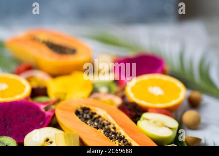 Set aus in Scheiben geschnittenen exotischen frischen Früchten. Verschiedene reife, saftige tropische Sommerfrüchte und tropische Blätter auf weißem Tisch. Selektiver Fokus. Horizontal Stockfoto