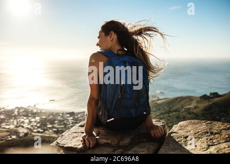 Rückansicht einer Frau mit Rucksack auf der Klippe sitzen und Blick auf die Aussicht weibliche Wanderer entspannen auf dem Gipfel des Berges. Stockfoto