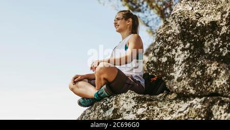 Frau, die auf dem Berg sitzt und wegschaut. Weibliche Bergsteigerin, die den Blick auf die Spitze des Berges schaut. Stockfoto