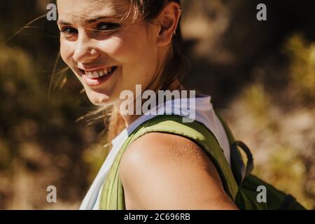 Nahaufnahme einer schönen Frau auf dem Bergweg. Bergsteigerin, die einen Berg besteigen und dabei die Kamera anschaut und lächelt. Stockfoto