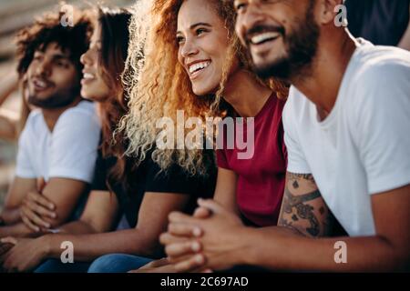 Junges Paar, das eine Sportveranstaltung im Stadion beobachtet. Multiethnische Gruppe von Sportfans, die im Stadion sitzen und ein Fußballspiel beobachten. Stockfoto