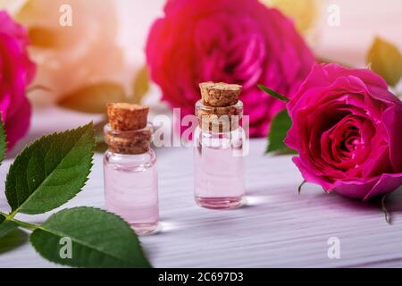 Parfümiertes Rosenwasser oder ätherisches Öl in Glasflaschen mit Blumen auf Holztisch Stockfoto