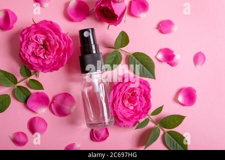 Rosenduft Spray mit rosa frischen Blumen und Blütenblättern auf rosa Hintergrund. Draufsicht Stockfoto