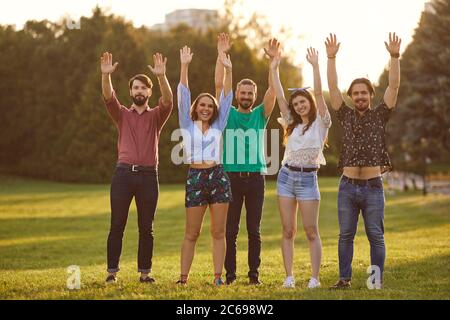 Eine Gruppe von Freunden hob fröhlich ihre Hände auf einer Picknick-Party in einem Sommerpark bei Sonnenuntergang. Stockfoto