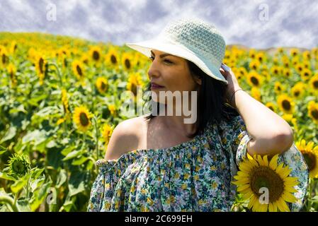 Schöne Frau trägt Hut und posiert in Sonnenblumenfeld Stockfoto