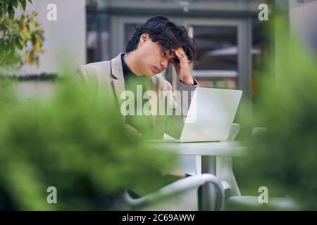 Müde junge Mann arbeitet auf Laptop im Café im Freien Stockfoto