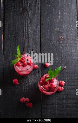 Frisch eiskalter Beerensaft-Drink mit Minze, Sommerlimonade in zwei Gläsern mit Strohhalmen auf dunklem Holzhintergrund, Draufsicht Kopierraum Stockfoto