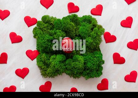 Rotes Ei im Moos und rote Herzen ringsum. Ostern festliche Konzept wuth Liebe. Stockfoto