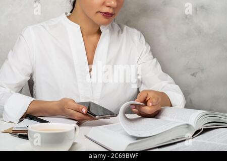 Studentin lesen Buch, suchen im Smartphone. Studing-Arbeitskonzept Stockfoto