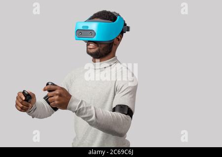 Afrikanische bärtiger Mann im VR-Brille fahren virtuelles Auto auf weißem Hintergrund lernen isoliert, ein Auto zu fahren. Virtuelle Fahrschule oder Studio Konzept Stockfoto