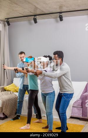 Spiel Gruppe junger multikulturellen diverse Freunde zu Hause mit Internet Technologie der virtuellen Realität Schutzbrille Headset. Männer, die Frauen der te zu meistern Stockfoto