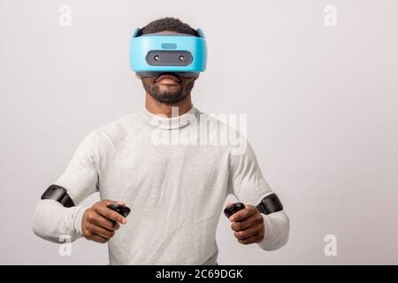 Dunkelhäutige zuversichtlich, dass man mit einer kurzen Stoppeln, pullower in Weiß gekleidet, trägt blaue mobile virtual reality Headset halten sich an den Händen, als ob Er fah Stockfoto