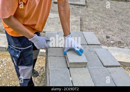 Der Meister legt neue Betonsteine für den Bürgersteig auf den Stapel. Die Steine wurden für die Verlegung eines neuen Fußweges vorbereitet. Stockfoto