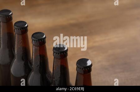 Bierindustrie. Reihe von dunklen Bierflaschen mit Kappen auf Holzhintergrund Stockfoto