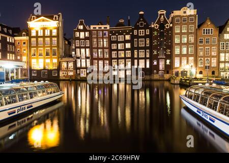 AMSTERDAM, NIEDERLANDE - 16. FEBRUAR 2016: Alte Gebäude am Damrak in Amsterdam bei Nacht. Boote und Reflexionen können gesehen werden. Stockfoto