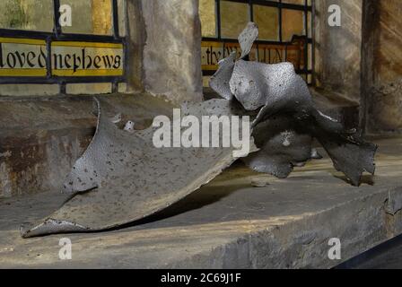 Verdrehter Scherbenhaufen aus Metallsplittern, der jetzt auf der Fensterbank in der Pfarrkirche Saint Laurence in Hawkhurst, Kent, England, UK, ausgestellt ist, ist der Rest der deutschen V1-Flugbombe, die im August 1944 während des Zweiten Weltkriegs auf dem Kirchhof explodierte. Viel altes Buntglas ausblasen und weitere Schäden verursachen. Obwohl die Kirche bis 1957 nicht vollständig repariert wurde, wurden später Teile des zerbrochenen Glases zu einem neuen Rundel gemacht und es profitierte auch von Schenkungen aus altem Glas von anderswo. Stockfoto