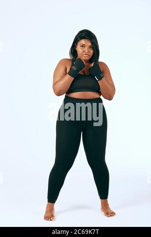 Plump Mulatto Frau in schwarzen Sportkleidung Ausübung, zeigt ihre Entschlossenheit, Gewicht zu verlieren. Isoliertes Studio auf Weiß. Stockfoto