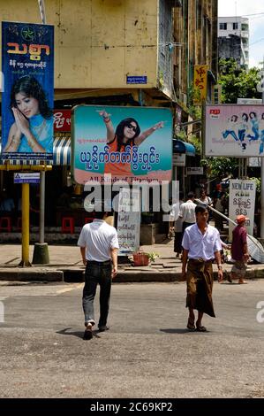 Zwei Männer überqueren die Straße in Yangon, einer in traditionellem Sarong, der andere in modernen Jeans. Myanmar. Stockfoto