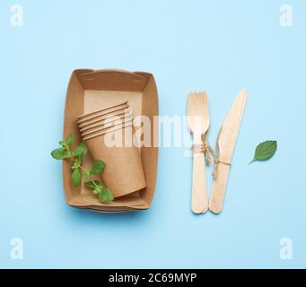 Pappteller und Tassen aus braunem Bastelpapier und Holzgabeln und auf blauem Hintergrund kniend. Kunststoff-Rückstoßkonzept, keine Verschwendung Stockfoto