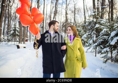 Schöne kaukasische Dame und Kerl in Mänteln feiern Jubiläum oder st Valentinstag zusammen. Sie im Winter Straße mit roten Luftballons, mit w Stockfoto